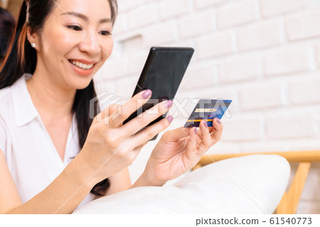 Face of 40s middle aged Asian woman holding credit card and mobile phone in cozy white room Face of 40s middle aged Asian woman holding credit card and mobile phone in cozy white room 61540773