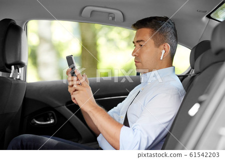 passenger with earphones and cellphone in taxi car 61542203