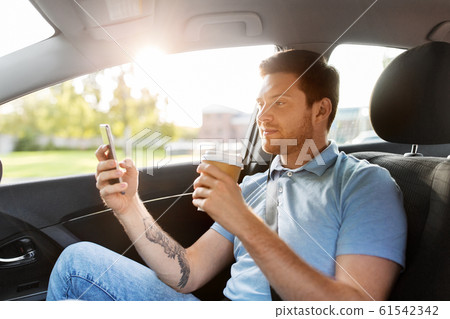 passenger drinking coffee using smartphone in car 61542342