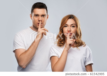 happy couple in white t-shirts making hush gesture 61542995