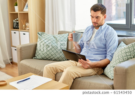 smiling man with tablet pc drinking coffee at home 61543450