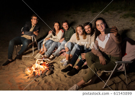happy friends taking selfie at camp fire on beach 61543899