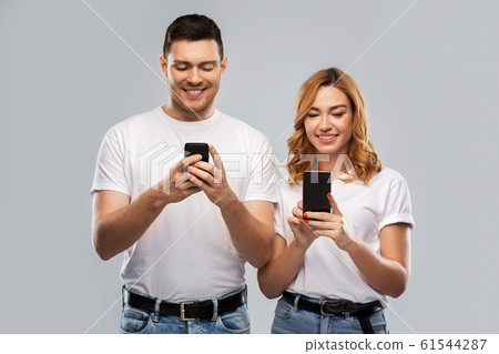 happy couple in white t-shirts with smartphones 61544287