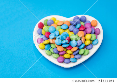 candies on heart shaped plate over blue background 61544564
