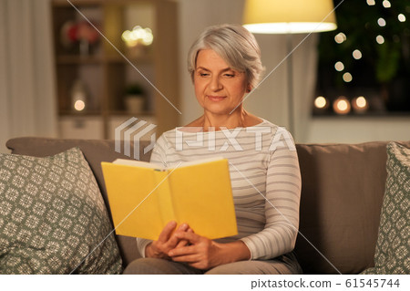 happy senior woman reading book at home in evening 61545744