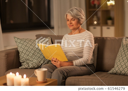 happy senior woman reading book at home in evening 61546279