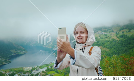 A happy tourist is photographed against the background of a picturesque fjord in Norway. It is worth on a popular photographic object - a flying cliff 61547098
