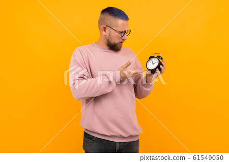 Young strong man with short black hair and glasses holds alarm clock and smiles Young strong man with short black hair and glasses holds alarm clock and smiles 61549050