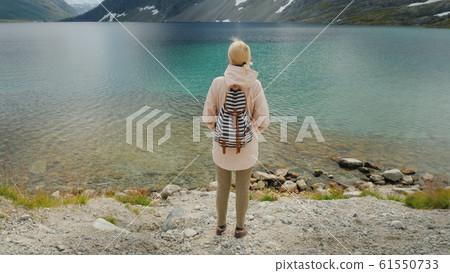 A woman admires a beautiful high mountain lake in the mountains of Norway. Crane shot A woman admires a beautiful high mountain lake in the mountains of Norway. Crane shot 61550733