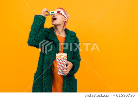 Extraordinary beautiful woman with short pink hair in dark coat and glasses eats popcorn isolated on Extraordinary beautiful woman with short pink hair in dark coat and glasses eats popcorn isolated on 61550750