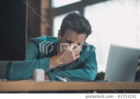 Unhappy cheerless man touching the bridge of the nose 61551242