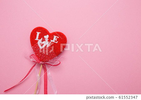 Closeup of a heart with a decor on a stick on a pink isolated background. Spell love in white letters. 61552347