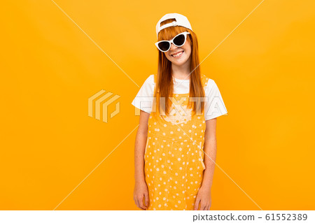 Pretty girl with red hair posing on camera and smiles with sunglasses isolated on yellow background 61552389