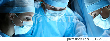 Group of surgeons at work operating in surgical theatre Group of surgeons at work operating in surgical theatre 61555396