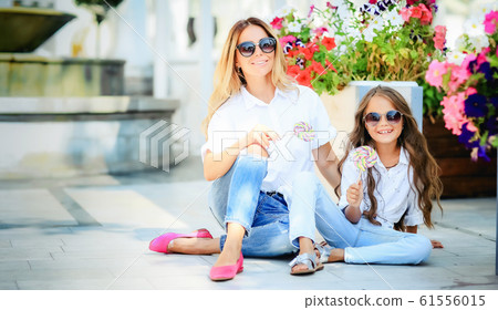 Fashion family concept - stylish mother and child wear. A portrait of a happy family: a young beautiful woman with her little cute daughter. Young daughter hugs mother in autumn city outdoor Fashion family concept - stylish mother and child wear. A portrait of a happy family: a young beautiful woman with her little cute daughter. Young daughter hugs mother in autumn city outdoor 61556015