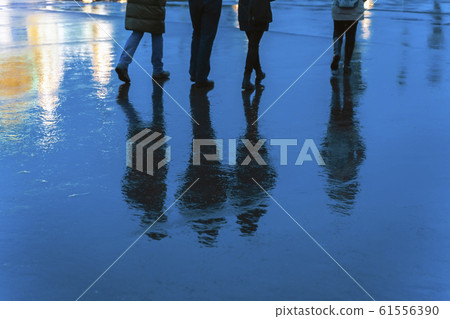 Blurry reflection legs and shadows, silhouettes of the men and women in the wet sidewalk, in a puddle, walk on a rain. Concept of seasons, weather, lifestyle 61556390