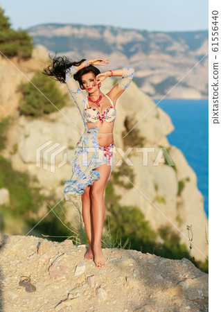 A woman in an Oriental dress stands on top of a cliff above the sea horizon A woman in an Oriental dress stands on top of a cliff above the sea horizon 61556440