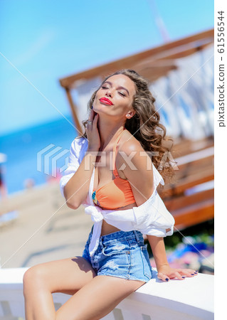 Portrait of a woman with curly long hair on the background of the sea and marine recreation areas Portrait of a woman with curly long hair on the background of the sea and marine recreation areas 61556544