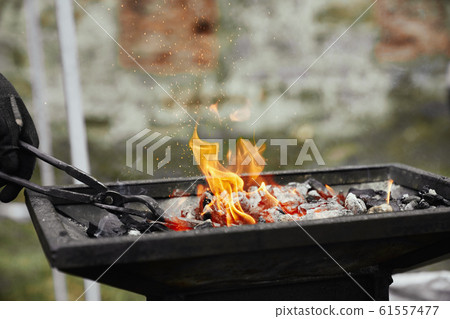 Blacksmith heating metal piece in burning coal. Blacksmith heating metal piece in burning coal. 61557477