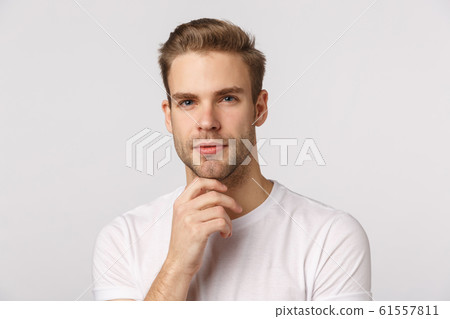 Hmm let me think. Pensive good-looking blond young bearded man in white t-shirt, touching chin and squinting intrigued, thinking, pondering what choice make, standing thoughtful Hmm let me think. Pensive good-looking blond young bearded man in white t-shirt, touching chin and squinting intrigued, thinking, pondering what choice make, standing thoughtful 61557811