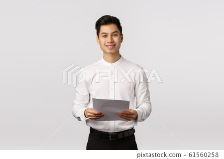 Handsome elegant asian young male coworker, businessman in white collar shirt, black pants, holding papers and smiling camera, successful entrepreneur prepare report, reading speech 61560258