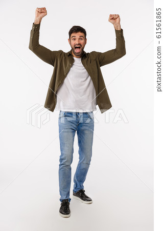 Success, achievement and victory concept. Vertical full-length shot glad and happy triumphing young bearded man in jeans and coat, raise hands up in hooray, win gesture, celebrating great news 61561865