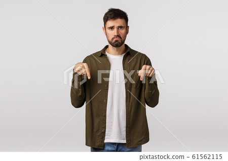 Man having disappointing bad news. Upset and miserable, unhappy young bearded man feeling regret or jealous, pulling sad grimace, frowning, pointing down complaining, white background Man having disappointing bad news. Upset and miserable, unhappy young bearded man feeling regret or jealous, pulling sad grimace, frowning, pointing down complaining, white background 61562115