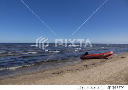 Rubber boat on a sand seashore on a blue sky background. 61562791