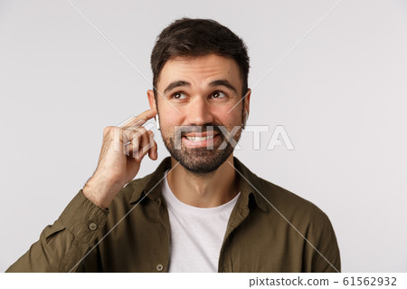 Carefree smiling handsome bearded adult male in coat, looking up dreamy and joyful, touching wireless earphone to tune in, change volume or finish call, standing white background happy Carefree smiling handsome bearded adult male in coat, looking up dreamy and joyful, touching wireless earphone to tune in, change volume or finish call, standing white background happy 61562932