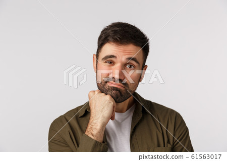 Bored and unimpressed, indifferent adult sad male with beard, looking reluctant and dissatisfied, lean head on fist, frowning, grimacing making indecisive upset expression, white background 61563017