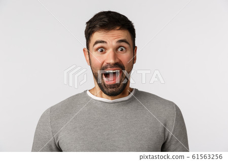 Extremely happy and cheerful good-looking bearded caucasian male in grey sweater, open mouth fascinated, say wow astonished and amused, visit amusement park, express awe and happiness 61563256