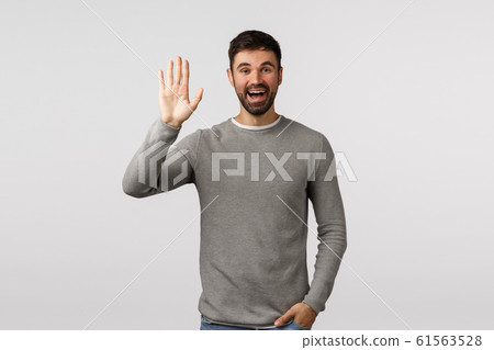 Friendly, cheerful and outgoing smiling bearded caucasian man, greeting neighbour raising arm and waving in hello, hi gesture, see person as waiting in meeting spot, standing white background 61563528