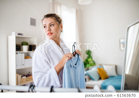 Young woman indoors at home in the morning, choosing clothes to wear. 61563670
