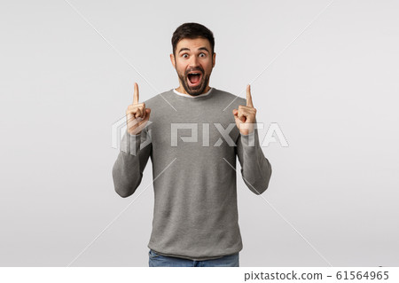 Happiness, overjoy and surprise concept. Astonished, speechless and wondered bearded boyfriend in grey sweater, see something amazing and unbelievable, pointing fingers up, promote offer Happiness, overjoy and surprise concept. Astonished, speechless and wondered bearded boyfriend in grey sweater, see something amazing and unbelievable, pointing fingers up, promote offer 61564965