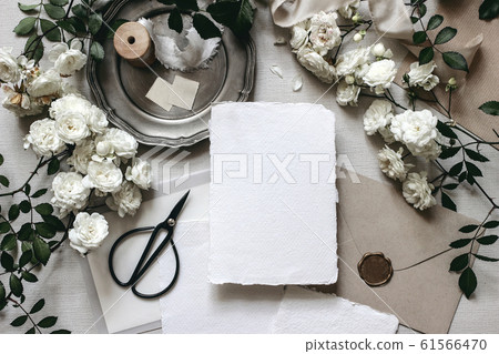 Moody wedding table mockup scene. Stationery composition with fading white rose flowers, silver plate, black scissors, envelopes and blank greeting cards. Grey textured background, flat lay, top view. 61566470