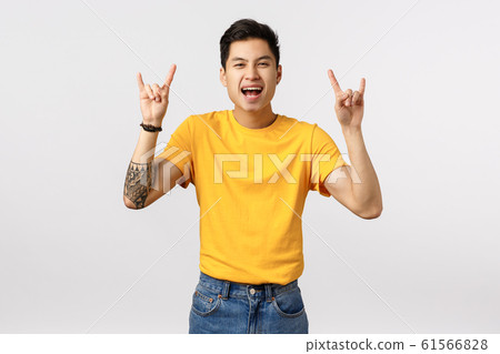 Rock-n-roll baby. Excited and playful good-looking asian tattooed hipster guy in yellow t-shirt, showing heavy metal gestures and screaming yeah thrilled, standing white background joyful 61566828