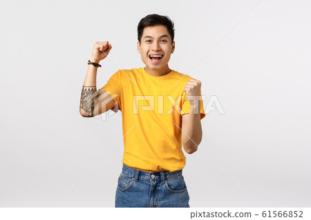 Hooray, well done good for you. Cheerful asian young tattooed man in yellow t-shirt, fist pump encouraging, rooting for player, placed bid, smiling rejoice, become champion, celebrating victory 61566852