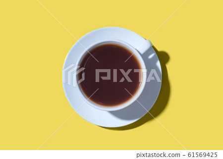 A cup of black coffee or tea on a yellow background. 61569425