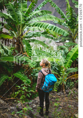 Blond young women with blue backpack admire banana plantation on the trekking route to paul valley on santo antao island, cape verde Blond young women with blue backpack admire banana plantation on the trekking route to paul valley on santo antao island, cape verde 61569770