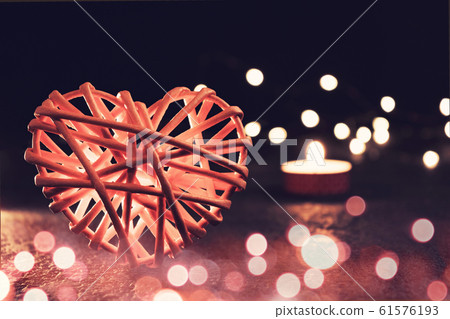 Romantic composition - one wicker heart is a symbol of love, lights and a burning candle on a dark table. Valentines day concept Romantic composition - one wicker heart is a symbol of love, lights and a burning candle on a dark table. Valentines day concept 61576193