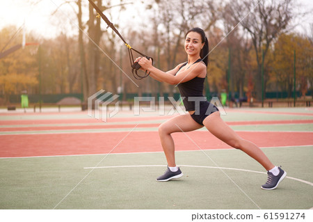 Girl athlete training using trx on sportground. 61591274