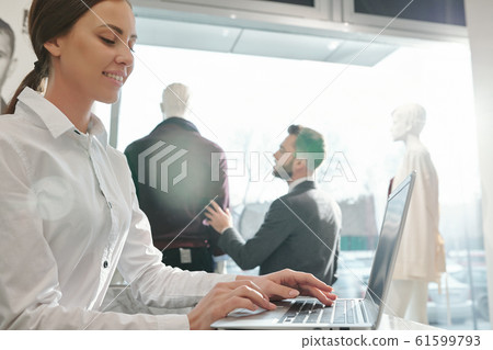 Young smiling shop assistant looking through online assortment on laptop screen 61599793
