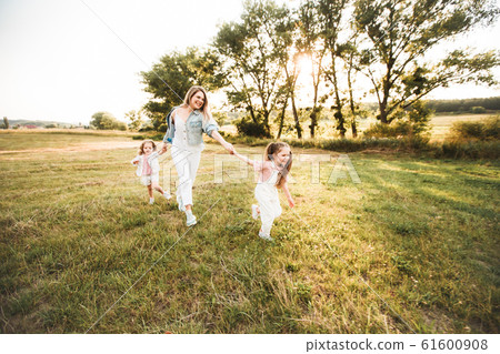 Blonde mother with two cute daughters are walking and having fun outdoors. Stylish, casual clothes. Blonde mother with two cute daughters are walking and having fun outdoors. Stylish, casual clothes. 61600908
