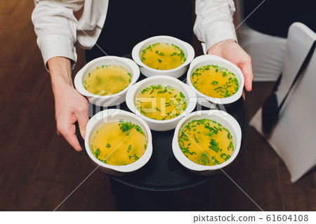 Waiter holding tray with plates of soup in the restaurant. 61604108