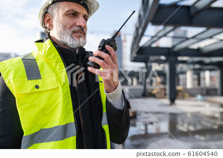 Man engineer using walkie talkie on construction site. Man engineer using walkie talkie on construction site. 61604540