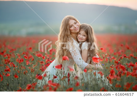 Young mom hugs daughter in field with bright red poppies Young mom hugs daughter in field with bright red poppies 61604657