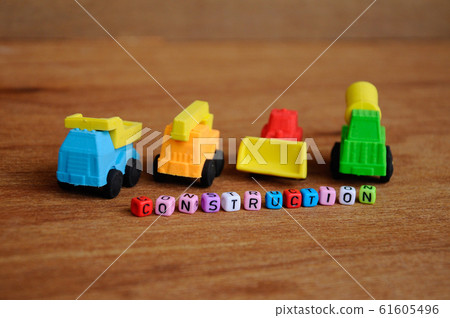 Miniature model of construction heavy machine made from synthetic rubber on wood texture background. Construction text printed on small plastic block in the middle. Miniature model of construction heavy machine made from synthetic rubber on wood texture background. Construction text printed on small plastic block in the middle. 61605496