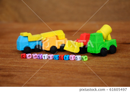 Miniature model of construction heavy machine made from synthetic rubber on wood texture background. Construction text printed on small plastic block in the middle. Miniature model of construction heavy machine made from synthetic rubber on wood texture background. Construction text printed on small plastic block in the middle. 61605497