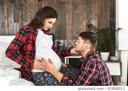 Beautiful pregnant couple in the bedroom. Preparing for childbirth, happy parents, waiting for the first child. Support for women before childbirth. 61608011