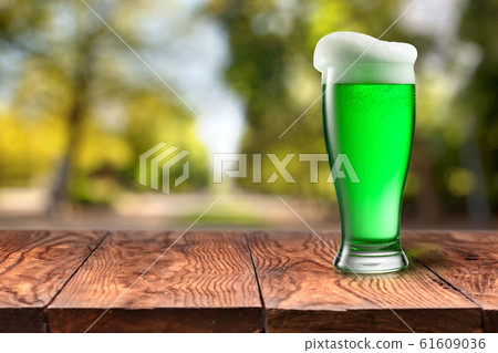 Green beer in glass on wooden table against blurred park. 61609036